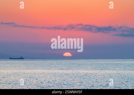 Sunrise view from Malaga seaside city in Andalusia, Spain, Europe. Serene sunrise over calm ocean waters, a lone vessel on the horizon. Stock Photo