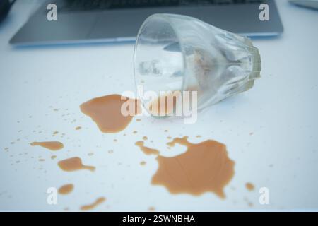 Coffee cup spills on a white table near a laptop at midday Stock Photo