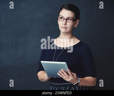 Business woman, web designer and thinking with tablet in studio for research or design on a dark background. Female person, thoughtful model or Stock Photo
