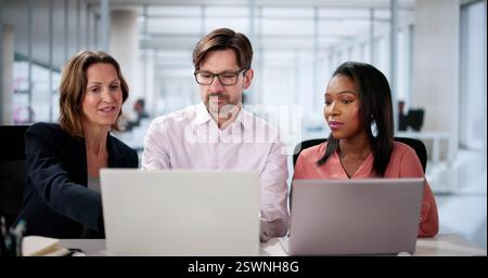 Diverse business team collaborating happily on laptop in office setting. Stock Photo