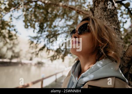 Woman in Sunglasses Leaning Against a Tree Stock Photo