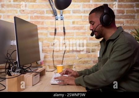 Focused programmer working on computer wearing headset in modern office Stock Photo
