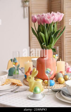 Festive table setting with vase of tulips, candles, painted eggs and Easter Stock Photo
