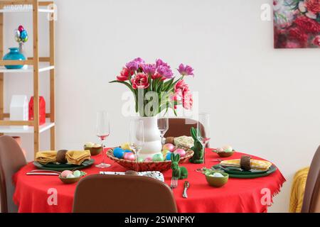 Festive Easter table setting with vase of flowers, cutlery, glasses and painted eggs Stock Photo