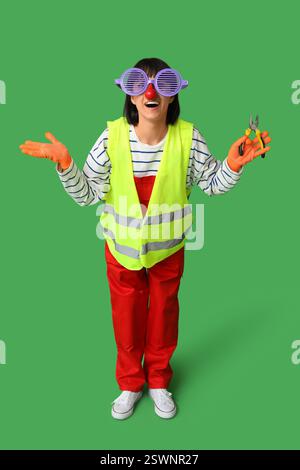 Young laughing female builder with pliers on green background. Fool's day Stock Photo