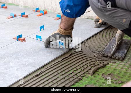 Bricklayer tiler installs tiles using leveling spacers. Construction industry. Building. Stock Photo