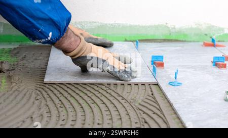 Bricklayer tiler installs tiles using leveling spacers. Construction industry. Building. Stock Photo