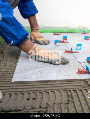Bricklayer tiler installs tiles using leveling spacers. Construction industry. Building. Stock Photo