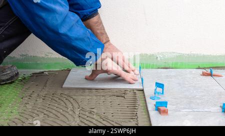 Bricklayer tiler installs tiles using leveling spacers. Construction industry. Building. Stock Photo
