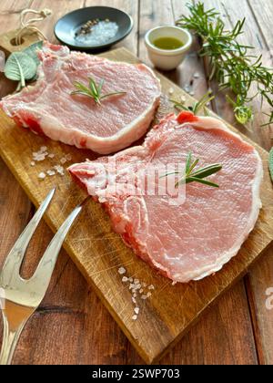 Raw pork steaks on the bone and herbs on a wooden cutting board. Fresh pork meat. Directly above. Stock Photo