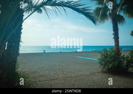 Low angle view of Almuncar beach through palm trees on a beautifully sunny day looking out to the horizon over the blue sea, beneath sunny blue skies Stock Photo