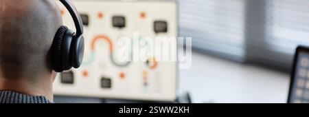 Website header shot bald male office worker shot from rear view listening to music with headphones while using computer at workplace, copy space Stock Photo