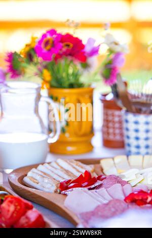 Brightly colored breakfast table with cheese, vegetables, and flowers in natural lighting. Stock Photo