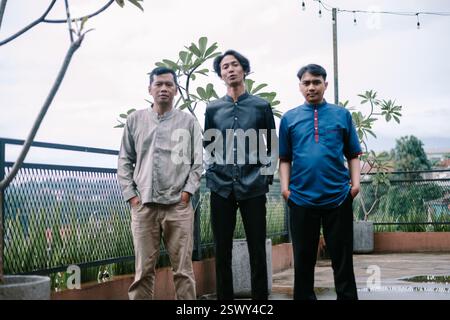 Three Indonesian men standing together on an outdoor rooftop. They are wearing various traditional muslim garments, representing diverse styles. They Stock Photo