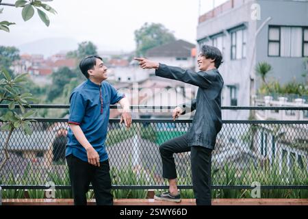 Two young men in casual attire are enjoying a lighthearted moment together. Set against an urban backdrop, they are smiling, gesturing, and engaging i Stock Photo