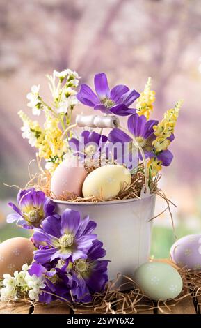 Easter eggs and flowers in a bucket on a wooden table with colorful springtime background Stock Photo