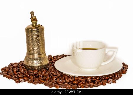 Vintage Hand Coffee Grinder with Ornate Metal Design and Classic White Coffee Cup on a Saucer, Surrounded by Roasted Coffee Beans Stock Photo