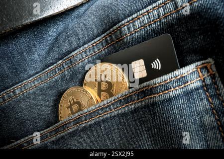 Credit card next to two Bitcoin physical coins inside a blue jeans pocket Stock Photo