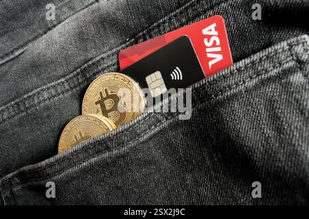 Venice, Italy - February 22, 2025: Credit cards from VISA next to two Bitcoin physical coins inside a black jeans pocket in Venice, Italy. Stock Photo