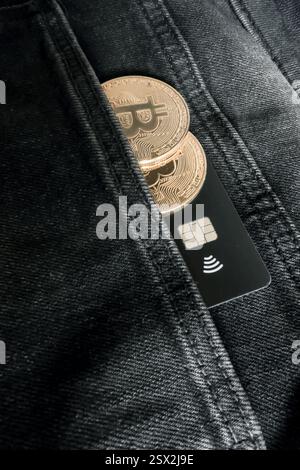 Credit card next to two Bitcoin physical coins inside a black jeans pocket Stock Photo