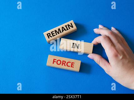 Remain in Force symbol. Concept words Remain in Force on wooden blocks. Businessman hand. Beautiful blue background. Business and Remain in Force conc Stock Photo