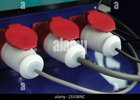 Three white and red electrical plugs are connected to a grey wire. The wires are connected to a device Stock Photo