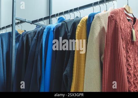 A rack of clothes with a blue sweater on top. There are many different colors and styles of clothing, including a red sweater, a yellow sweater, and a Stock Photo