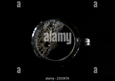 Top view of a glass cup filled with black coffee, featuring frothy bubbles on the surface, against a dark background. Minimalist coffee concept. Stock Photo