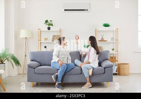 Climate control couple air conditioner fixing sitting relaxing on sofa holding controller, regulate  Stock Photo