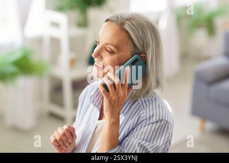 Senior happy mature woman retired engaged in pleasant talk on phone holding gadget close to ear Stock Photo