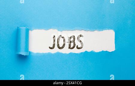 jobs word written on torn paper on blue background Stock Photo