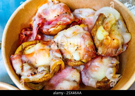 Delicious potato cups filled with melted cheese and wrapped in crispy bacon are served in a brown bowl, showcasing a tempting dish perfect for sharing Stock Photo