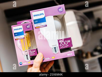 Paris, France - Feb 17, 2025: A person holds two Philips LED light bulbs in their original packaging, featuring cool white 4000K light, high wattage e Stock Photo