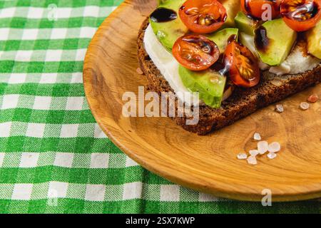 A delicious serving of whole grain toast is topped with creamy cheese, ripe avocado slices, and halved cherry tomatoes. The dish is presented on a rus Stock Photo