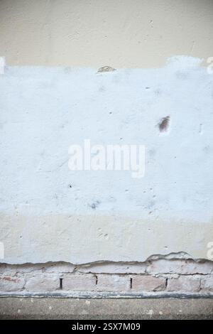 Cremona, Italy February 9th 2025 Close up of a weathered wall revealing layers of paint, exposed brick, and a concrete base, showcasing the passage of Stock Photo