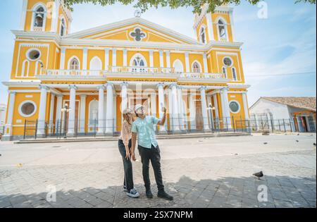 Young tourist couple taking selfies at the cathedral in Granada, Nicaragua. Happy tourist couple taking selfies in a colorful colonial cathedral Stock Photo