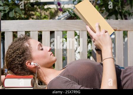 Young woman sits on a bench and reads a book Stock Photo