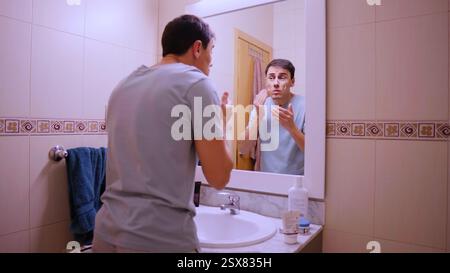Man applying face cream in bathroom mirror Stock Photo