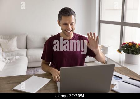 Young man greeting videocall participant sitting at table at home Stock Photo