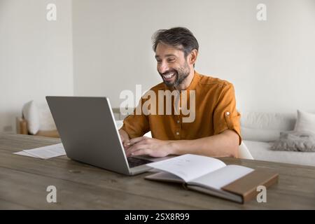 Happy middle-aged man sitting at table using laptop Stock Photo