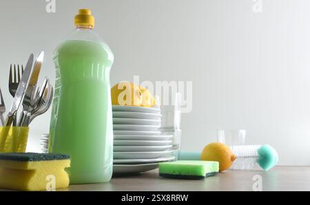 Eco-friendly dishwasher for washing dishes with bottle full of product, scouring pads and stack of plates with lemons on wooden kitchen bench and whit Stock Photo
