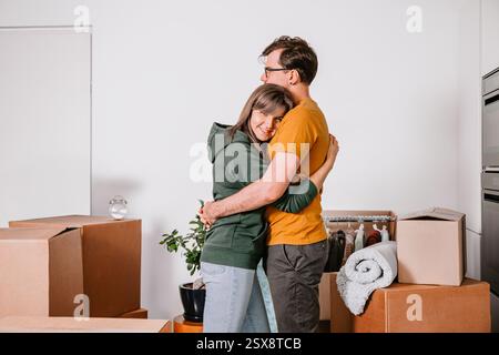 A loving couple shares a warm hug while moving into their new home, surrounded by packed boxes, fresh start together Stock Photo