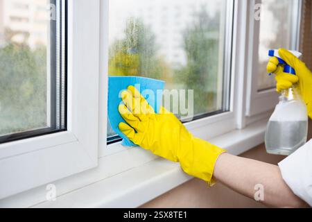 Householder man in yellow rubber gloves sprays glass cleaner and wipes the window with sponge, spring window cleaning Stock Photo