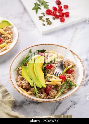 Plate with porridge from crushed buckwheat groats with avocado, apples, dried cherries and salad on table Stock Photo