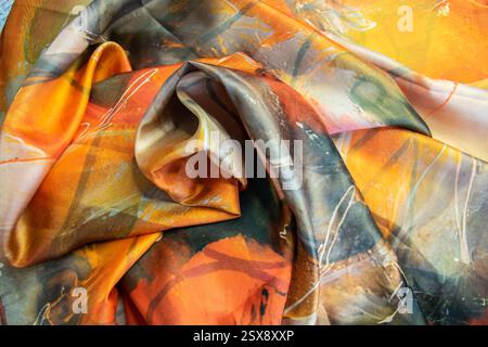 Beautiful textile silk scarf. Yellow, orange, brown handmade texture fabric. Cloth background. Stock Photo