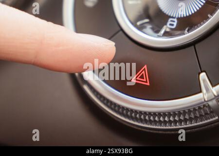 A detailed closeup shot showing a hand firmly pressing the hazard light button located on a car dashboard. The activation of hazard lights from the ca Stock Photo