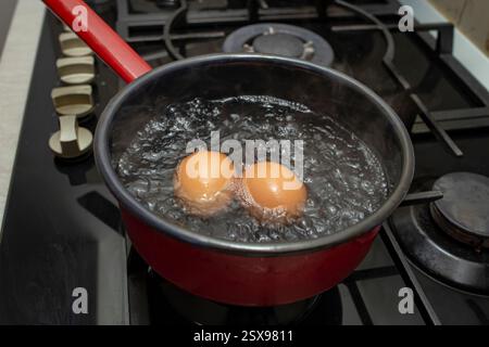 Two orange eggs boiling in a  black pot with bubbles and steam, soft focus Stock Photo