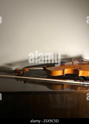 A violin and a bow lying on top of the vintage black piano in the concert hall in the evening, white wall, playing music, art, performance, lifestyle. Stock Photo