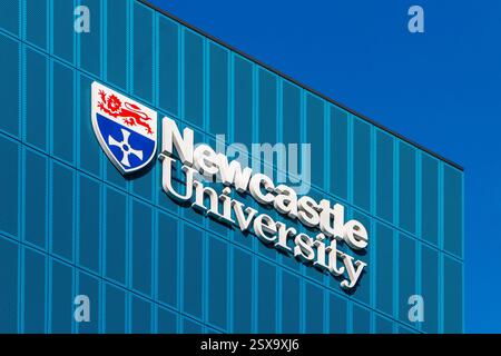 Modern exterior view of Newcastle University building with its prominent logo against a clear blue sky Stock Photo