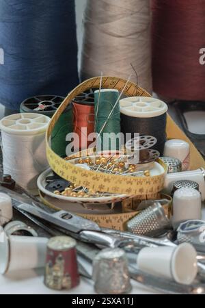 Sewing needles stuck in a green miniature spools thread Steel scissors, Spools of thread of various colour, Thimbles and Measuring tape including Pins Stock Photo